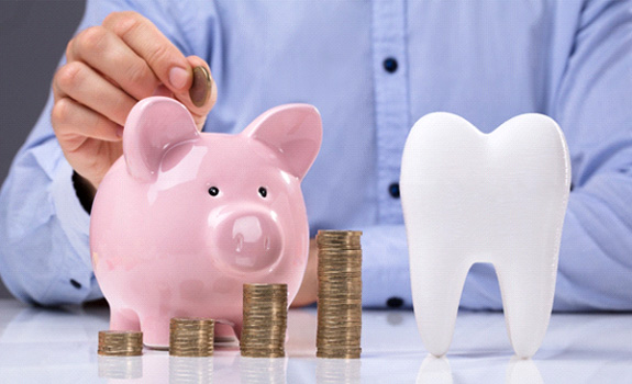 Model of tooth next to piggy bank and stacks of coins