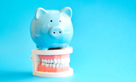 Piggy bank atop model teeth representing the cost of Invisalign in Rockwall