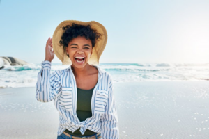 Woman in sunhat laughing in the sun, ocean waves behind her